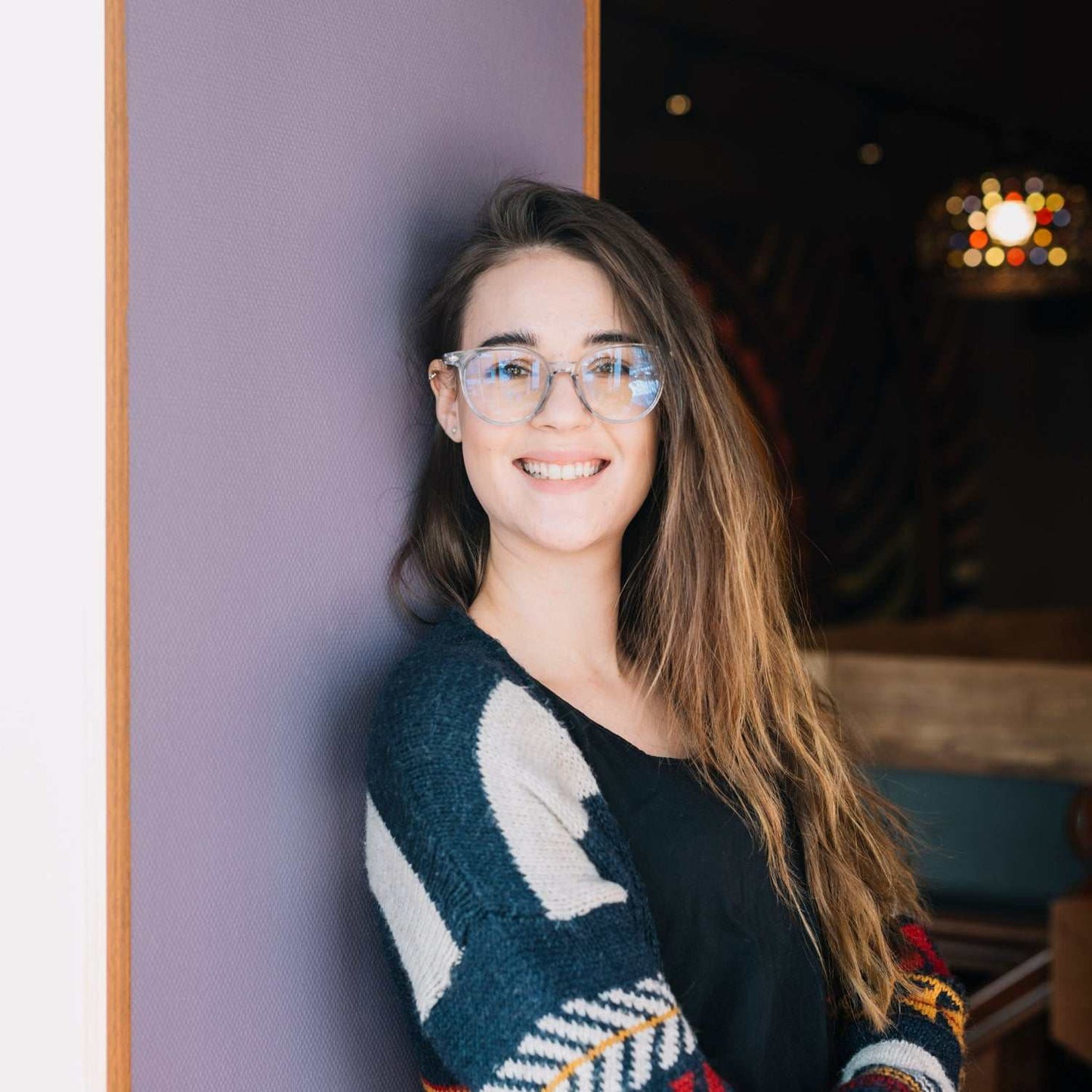 Young woman smiling wearing glasses and a cozy sweater indoors, representing women's health and wellness.
