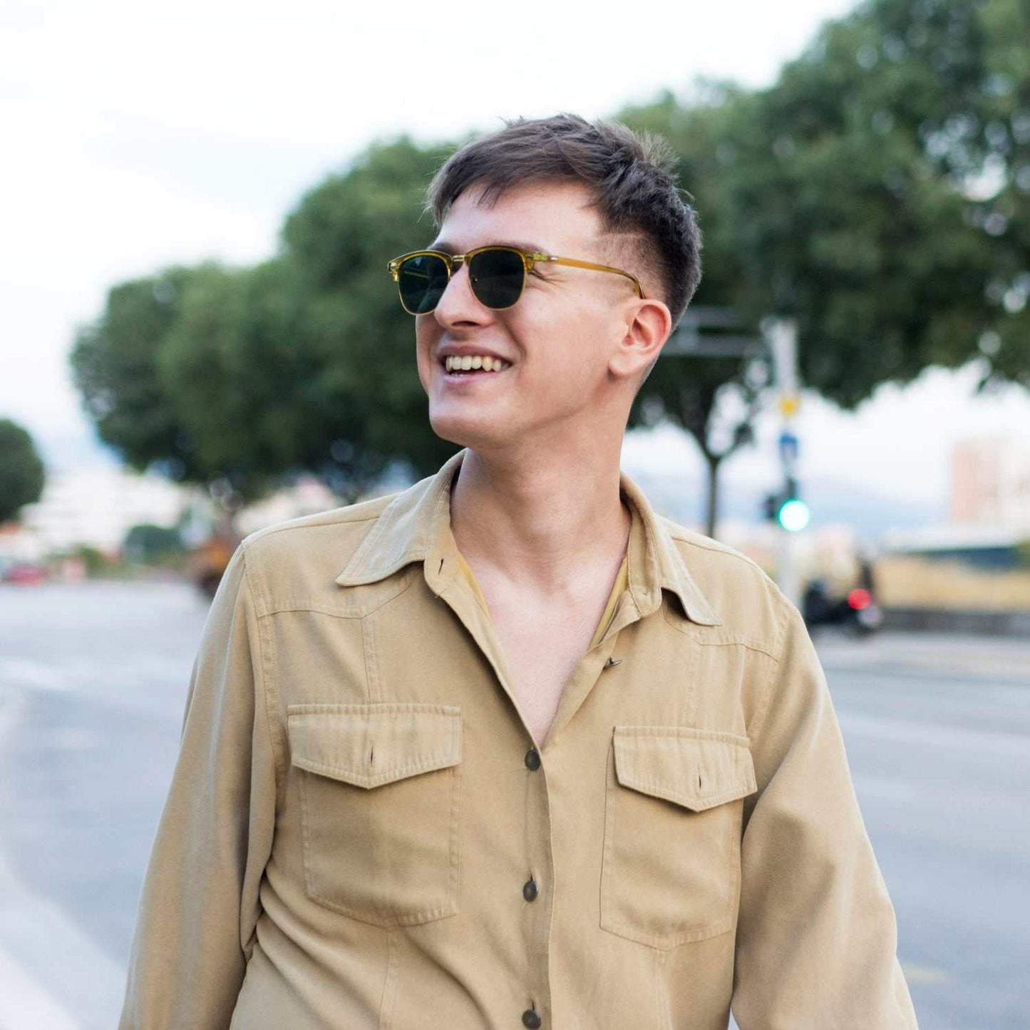 Young man smiling outdoors wearing sunglasses and casual beige shirt representing male preventive health checkup under 40 years