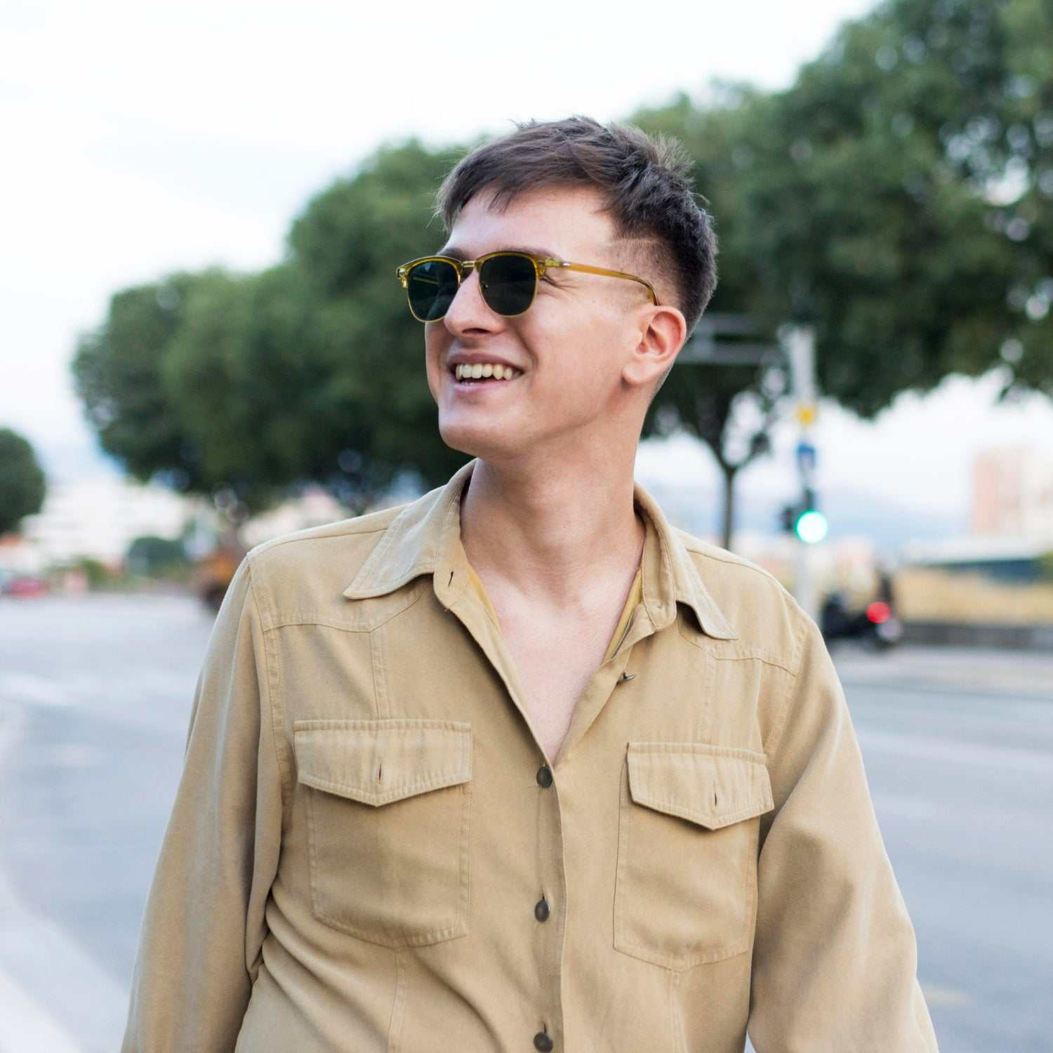 Young man smiling outdoors wearing sunglasses and casual beige shirt representing male preventive health checkup under 40 years