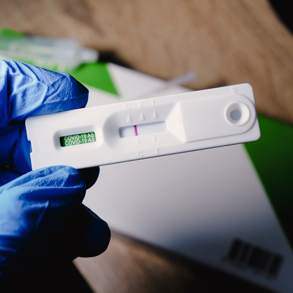 Hand with blue glove holding a rapid antigen COVID-19 test cassette showing test results